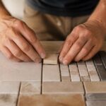 Dłonie układające płytki ceramiczne w mozaikowy wzór na stole roboczym